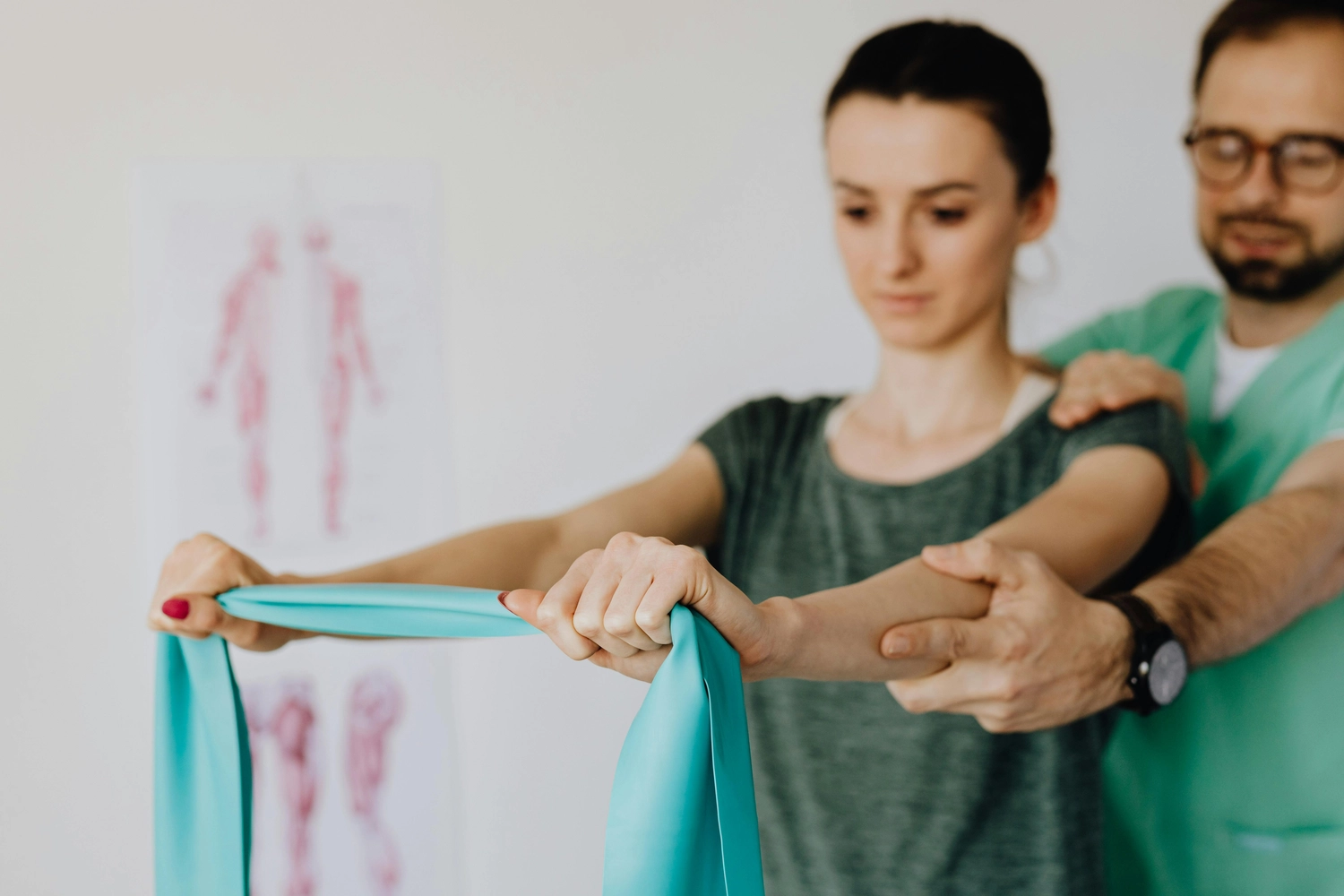 Osteopathie am Park – Ganzheitliche Behandlung – Dieses Bild zeigt einen Physiotherapeuten, der einen Patienten bei einer Rehabilitationsübung mit einem blauen Widerstandsband unterstützt, die wahrscheinlich der Kräftigung des Oberkörpers oder der Verbesserung der Schulterbeweglichkeit dient.